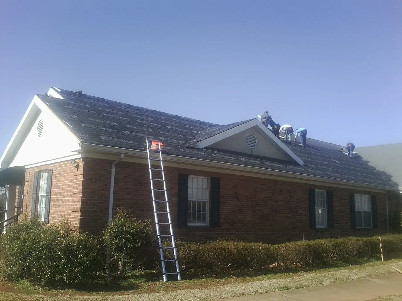 Crew tearing shingles off a brick ranch roof with a ladder set — Emergency Roof Repair work by our crew in Howard Lake