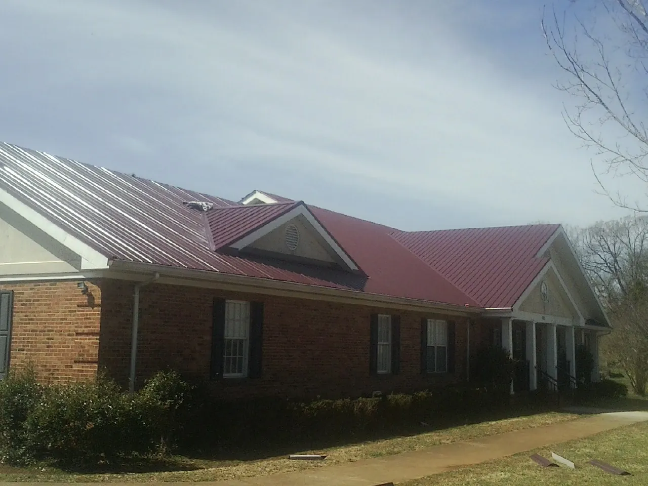 Red metal roof with gabled entries on a long brick building, from a Hail Damage Roof Repair job in Howard Lake