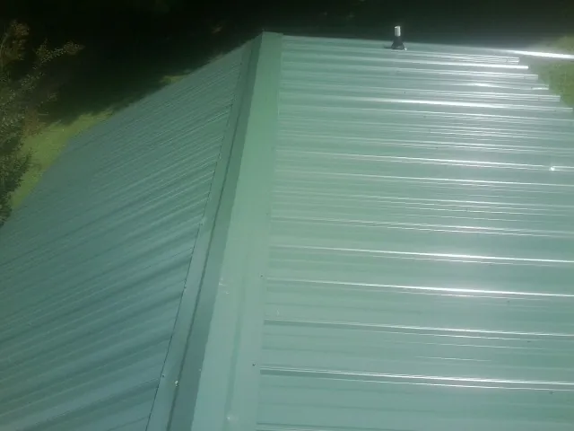 New green metal panels meeting at the ridge of a roof — Flat Roof Repair work by our crew in Howard Lake