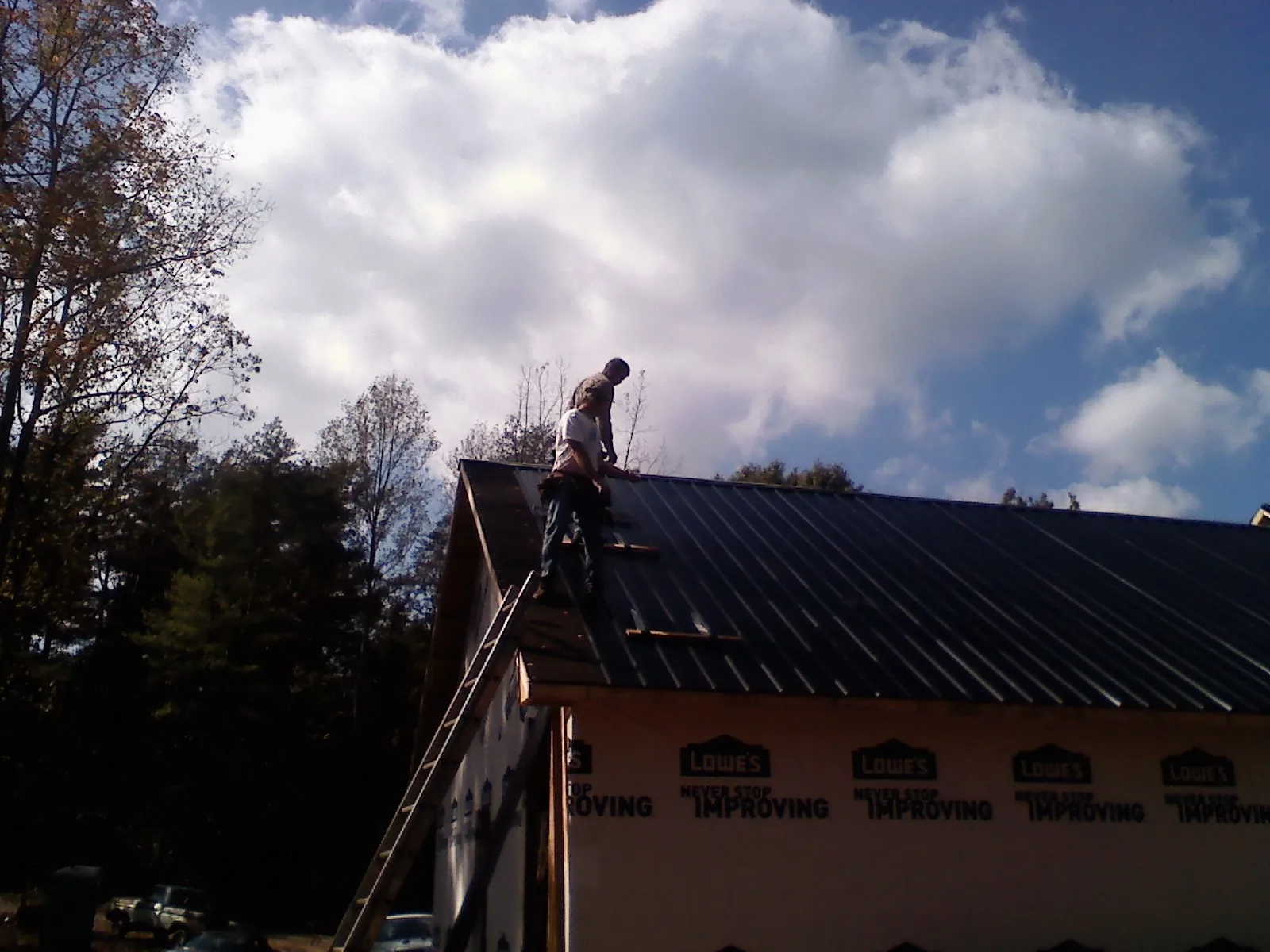 Roofer fastening dark metal panels high against a cloudy sky, from a Roof Inspection job in Howard Lake
