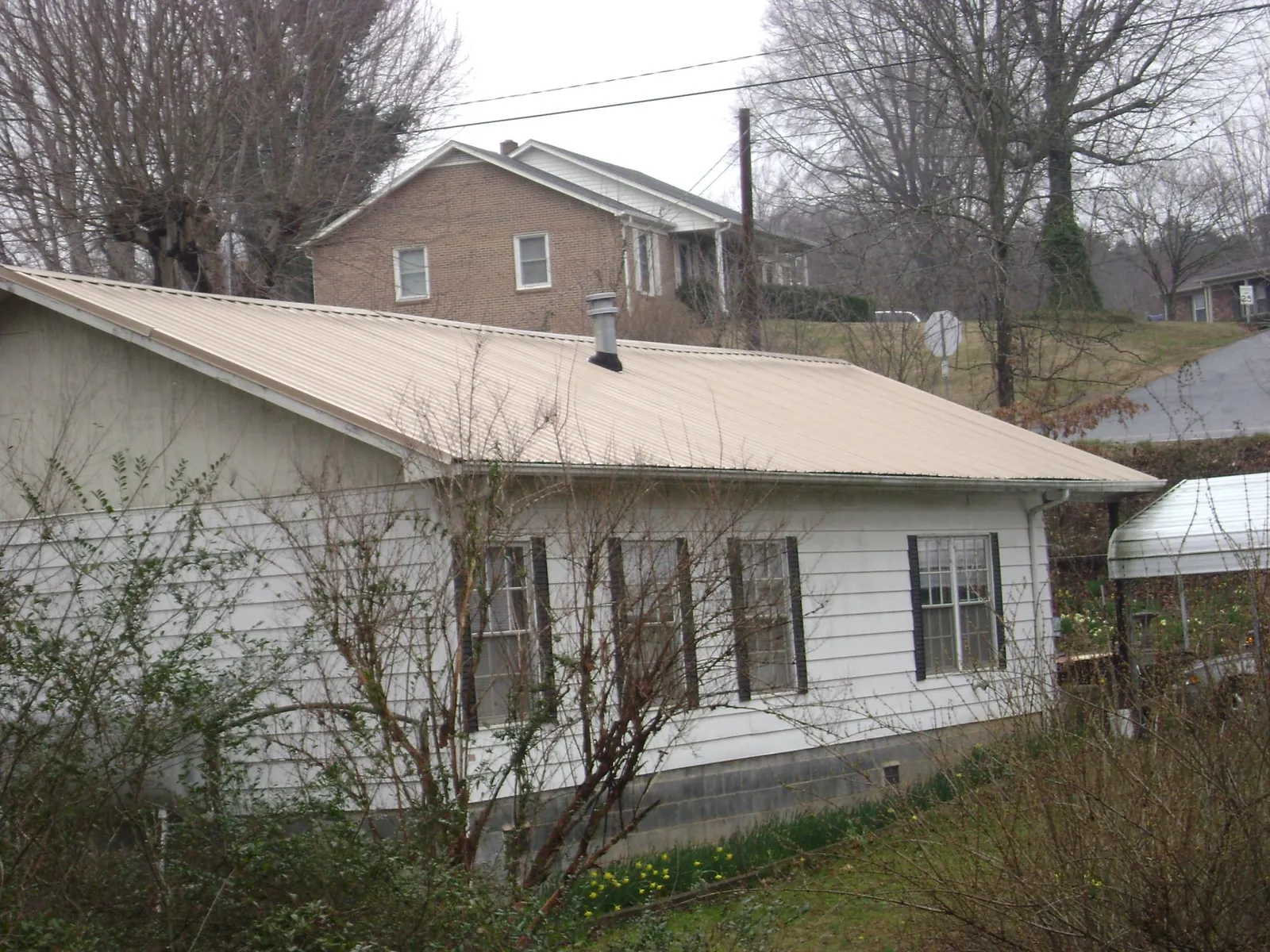 Tan metal roof on a white sided house set into a hillside — Commercial Roofing by Roofing Brothers in Howard Lake