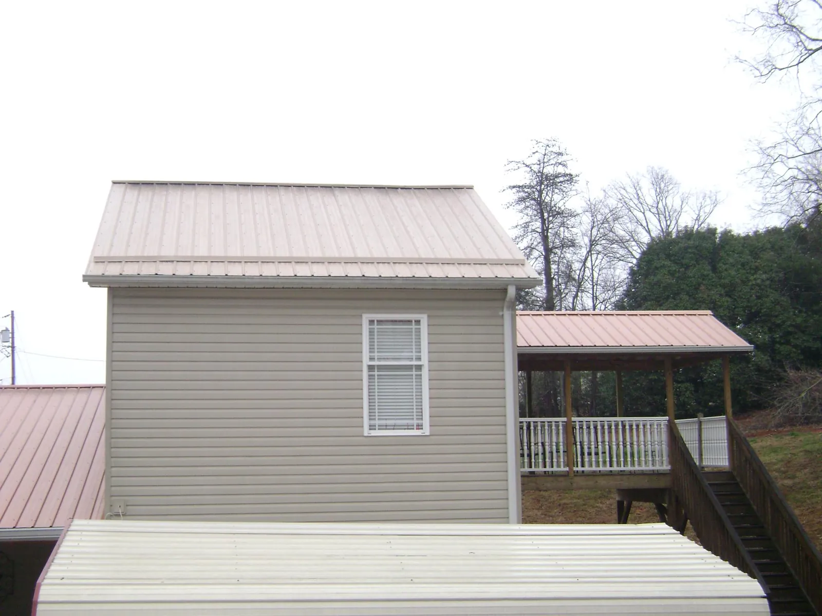 Tan metal roofs on a two story addition and attached porch, from a Roof Replacement job in Howard Lake